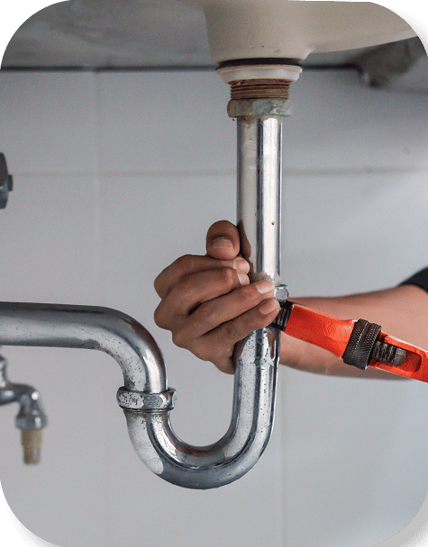 Plumber's hands working on a pipe under a sink